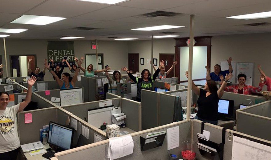 Group of team members standing with arms in the air in their cubicles