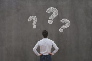 man looking at a chalkboard with three question marks