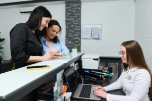 receptionist working at the front computer with patients at the desk